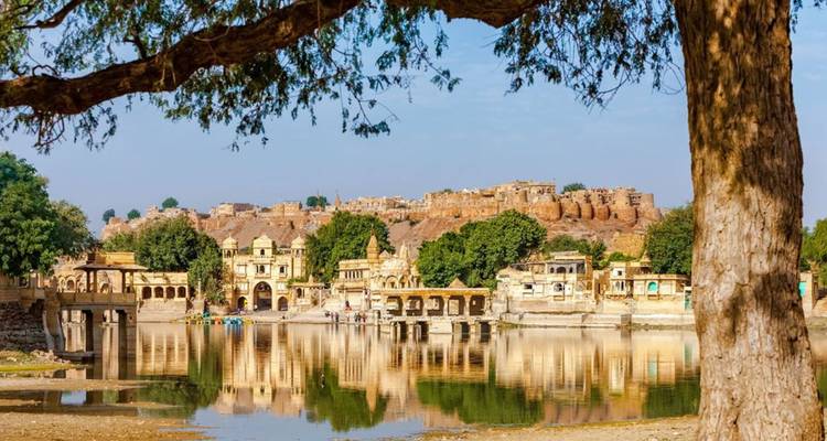 Ruhiger See spiegelt goldene Festungsmauern und Stadtgebäude wider, gerahmt vom Ast eines Baumes im Vordergrund.
