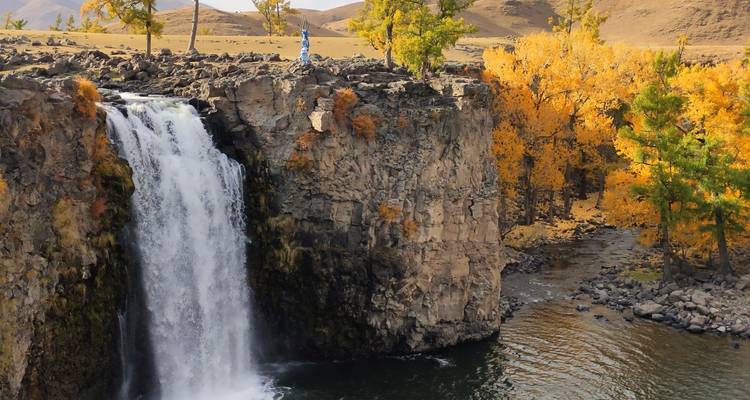Une puissante cascade dévale une falaise de basalte entourée d'arbres dorés d'automne dans un bassin sombre.