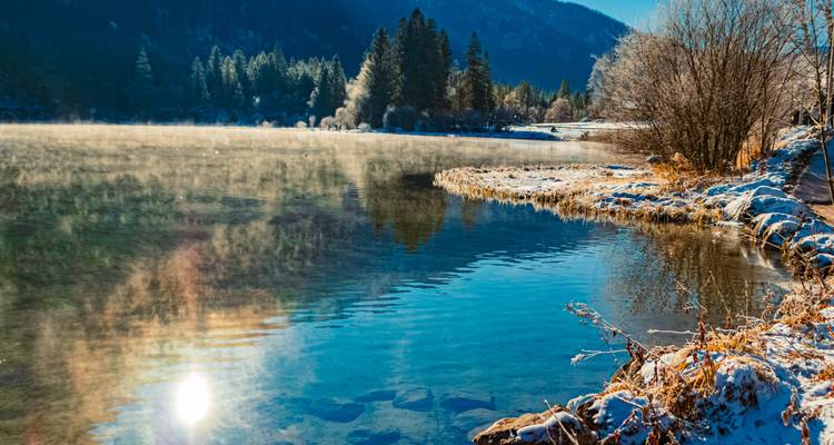 Lac cristallin reflétant la végétation givrée du rivage avec de la brume s'élevant contre les montagnes boisées
