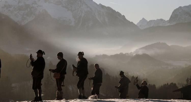 Silhouettes de musiciens alpins jouant des cors traditionnels sur fond de montagnes brumeuses