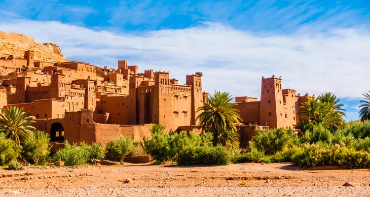 Ciudadela fortificada de adobe de Ait Ben Haddou que se eleva sobre una línea de palmeras bajo un cielo azul intenso.