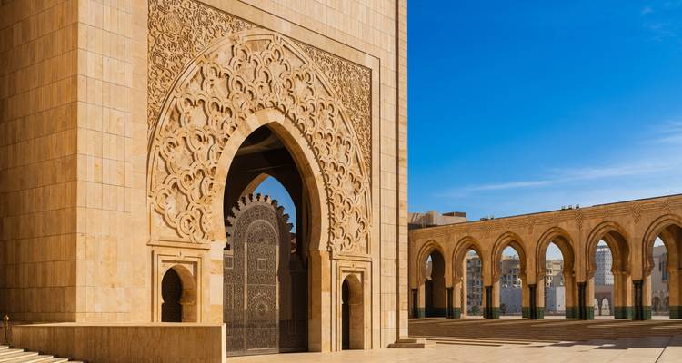 Arco intrincadamente tallado y entrada ornamentada de la Mezquita Hassan II resplandeciendo contra un cielo azul despejado.