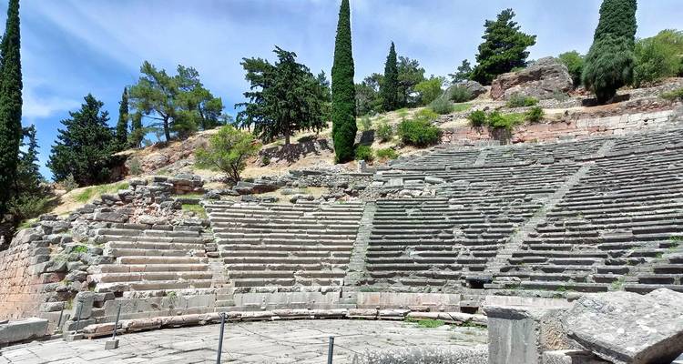 Un amphithéâtre de pierre ancienne dont les gradins épousent les courbes d'une colline au milieu de cyprès et de pins.