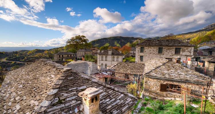 Maisons aux toits de pierre d'un village de montagne traditionnel éparpillées sur une colline verdoyante sous des nuages dramatiques.