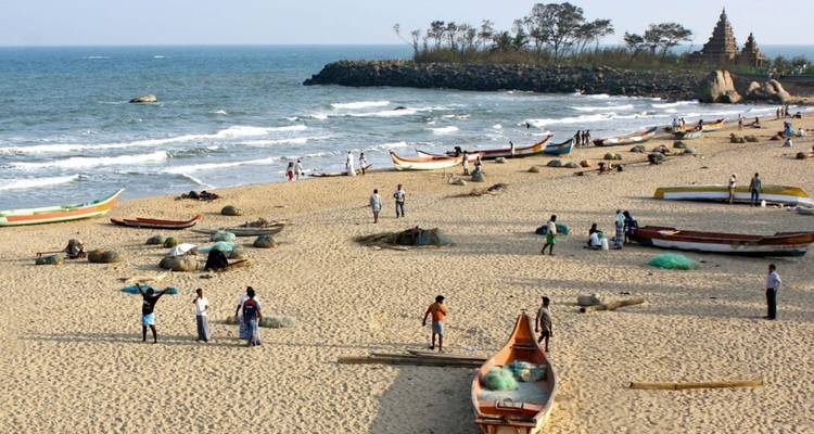 Breiter Sandstrand mit Fischerbooten und Einheimischen, mit dem Küstentempel in der Ferne sichtbar.