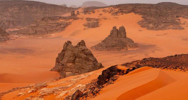 Vast orange dunes and sculpted sandstone outcrops stretching across a remote desert landscape