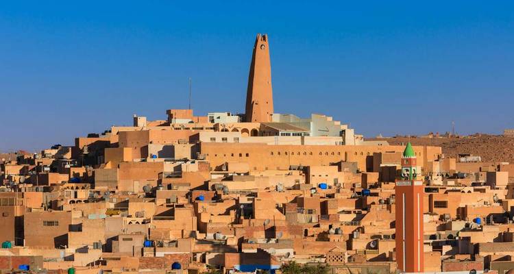 Sun-baked adobe city crowned by a tall slender minaret against a deep blue sky
