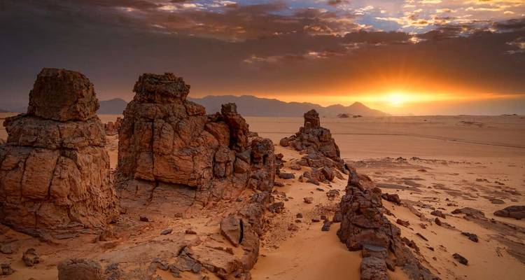 Golden sunset illuminating dramatic rock pinnacles and vast sandy plain in the Sahara
