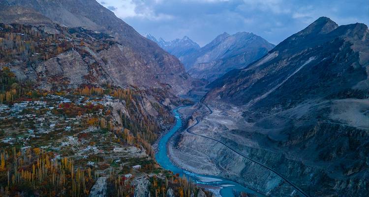 Une vue aérienne au crépuscule d'une rivière turquoise serpentant à travers des montagnes escarpées et des villages en terrasses.