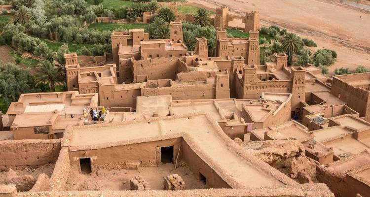 Luftaufnahme über die Lehm-Ksar von Ait Benhaddou neben einer grünen Oase.