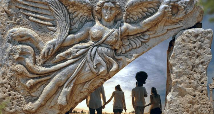 Relief de la déesse ailée Niké encadré par les silhouettes de trois visiteurs en dessous