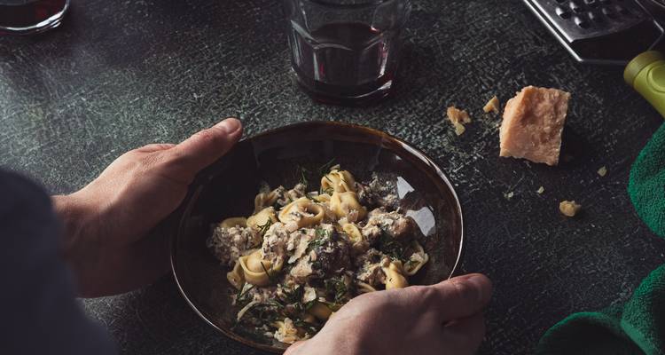 Bol rustique de pâtes tortellini garnies d'herbes à côté d'un verre de vin rouge à moitié rempli.