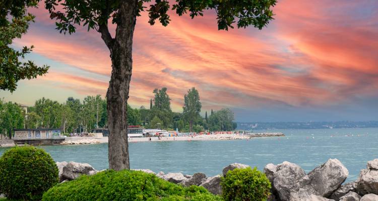 Des nuages de coucher de soleil roses et oranges spectaculaires se reflètent sur les eaux calmes du rivage du lac de Garde.