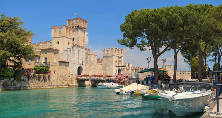 Les tours crénelées du château Scaliger se reflètent dans les eaux turquoise des douves par une journée ensoleillée à Sirmione.
