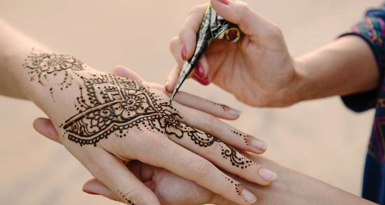 Nahaufnahme von aufwändigem Henna, das mit einem traditionellen Kegel auf eine Hand aufgetragen wird.