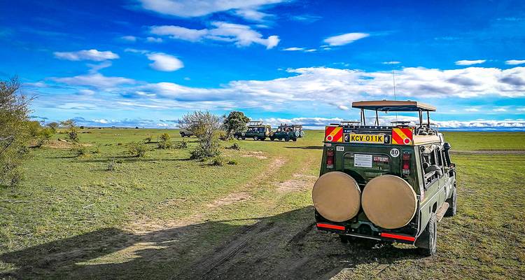 Safarauto's doorkruisen open savanne onder een uitgestrekte blauwe hemel met verspreide wolken