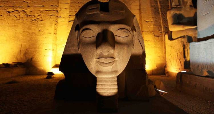 Illuminated pharaoh head statue at night inside Luxor Temple with warm golden lighting