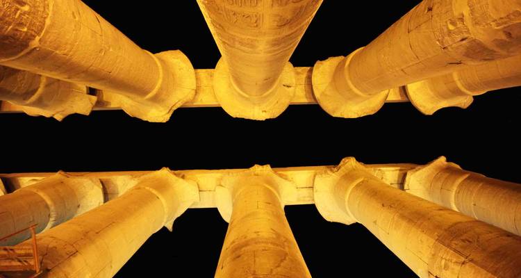 Nighttime perspective of dramatically lit Egyptian temple columns rising against a black sky.