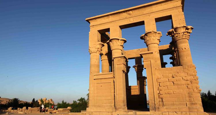 Sandstone columned pavilion of an ancient temple bathed in golden light beneath a clear sky.