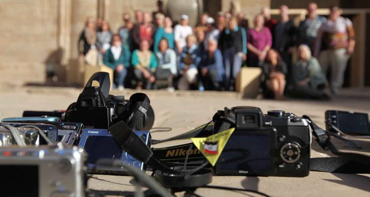 Cameras in sharp focus lie on stone ground while a blurred tour group poses for a background photo.