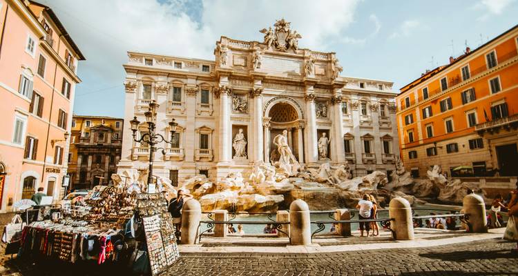 Scène animée à la Fontaine de Trevi de Rome avec des visiteurs et des stands de souvenirs installés au milieu de sculptures baroques ornées.