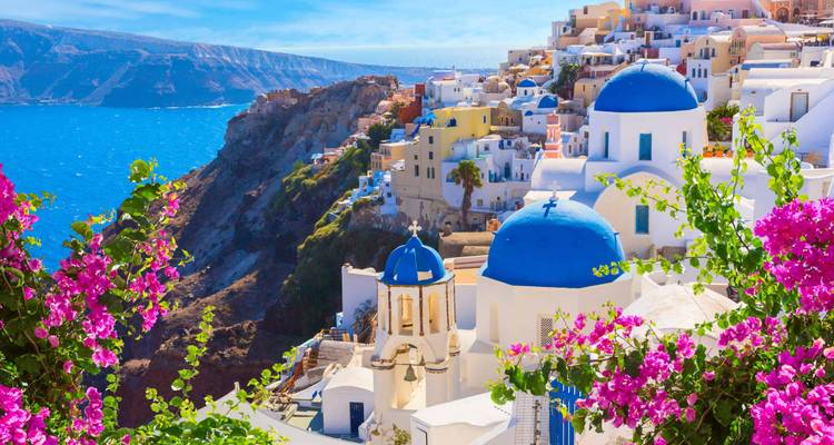 Scène classique de Santorin avec des églises aux dômes bleus, des bâtiments blanchis à la chaux et des bougainvilliers roses éclatants surplombant la mer Égée.