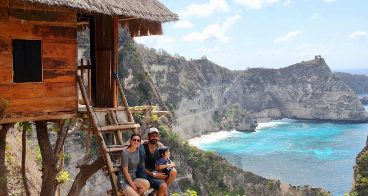 Famille assise sur une cabane dans les arbres rustique au bord d'une falaise surplombant une baie d'un bleu éclatant