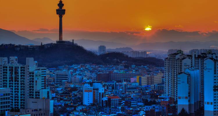 Paysage urbain de Daegu au coucher du soleil avec la tour 83 se détachant en silhouette contre un ciel orange.