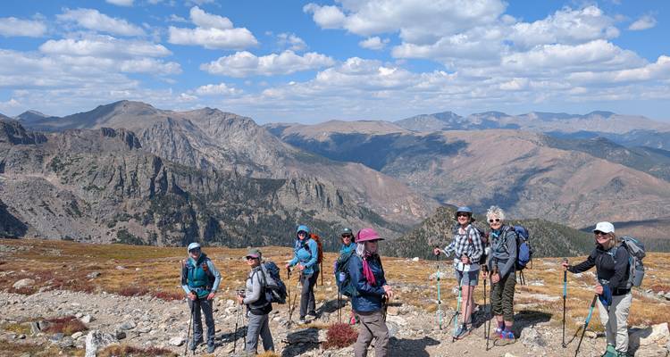 Groupe de randonneurs avec bâtons de marche admirant de vastes panoramas montagneux sous des nuages épars.
