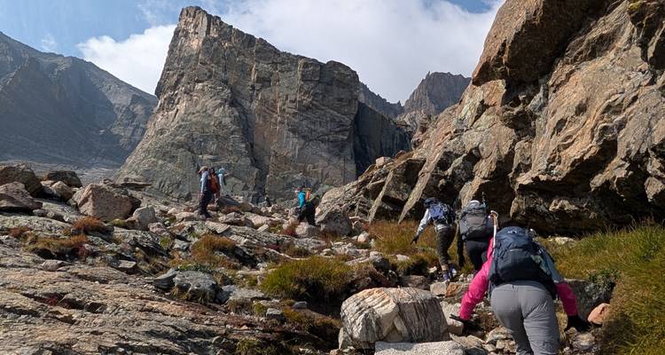 Des randonneurs grimpant sur un flanc de montagne rocheux et accidenté vers de hautes parois de pierre et un ciel bleu.