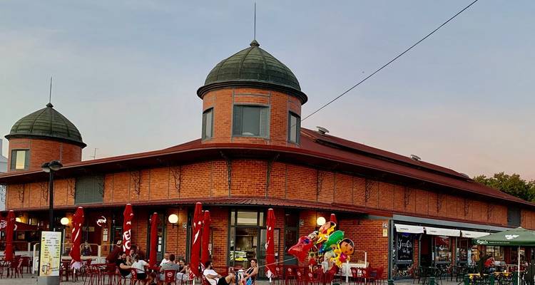 Les gens dînent à l'extérieur du bâtiment historique du marché d'Olhão en briques rouges sous un ciel pastel du soir.