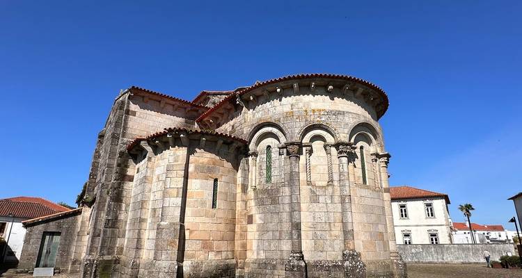 Eine gut erhaltene romanische Steinkirche mit gerundeten Apsiden steht unter einem klaren blauen Himmel