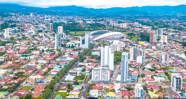 Vue aérienne de San José avec le stade national et les montagnes lointaines sous un ciel lumineux.