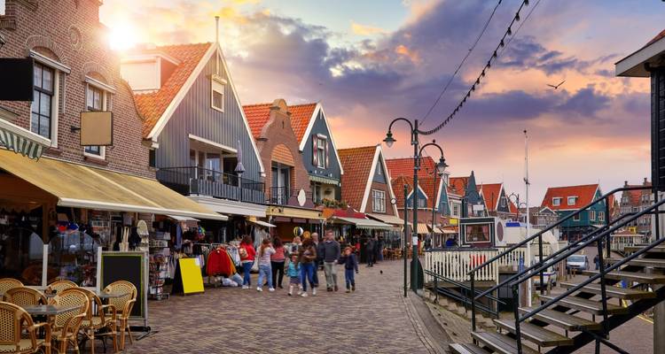 Pintoresca calle comercial en Volendam con casas tradicionales holandesas de hastiales, tiendas y turistas paseando bajo un cielo nocturno dramático.