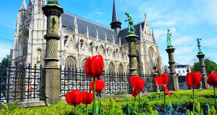 Gotische Kirche in Brüssel, eingerahmt von leuchtend roten Tulpen und dekorativen Säulen an einem sonnigen Tag