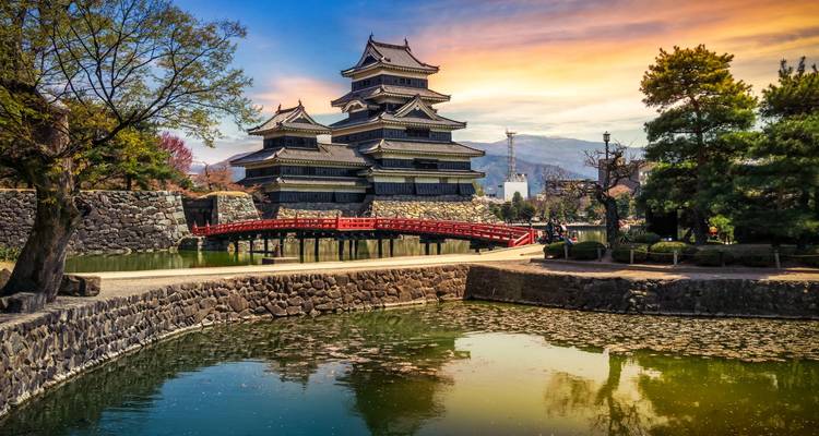 Resplandor del atardecer sobre el Castillo de Matsumoto con un puente rojo y el foso de agua tranquila.