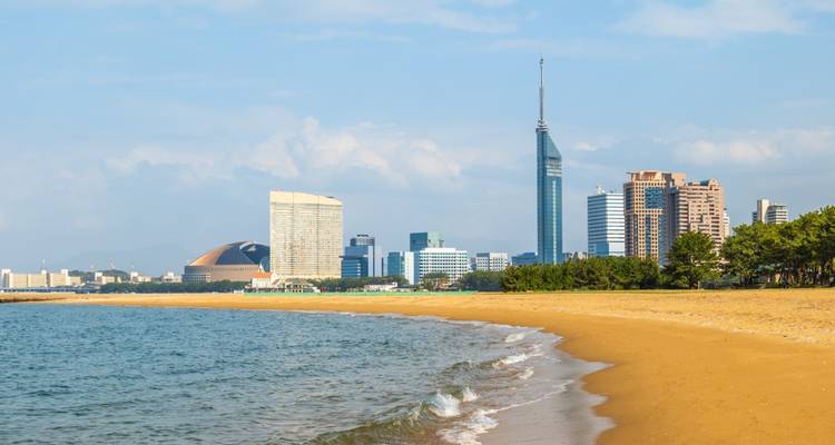 Plage de sable courbant vers un horizon moderne avec la tour de Fukuoka au bord d'une mer bleue calme.