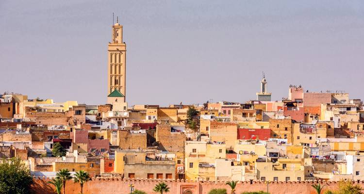 Paisaje urbano de Meknes con un prominente minarete beige que se eleva sobre casas compactas de tonos tierra.