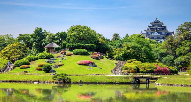 Colina de jardín vibrante frente al Castillo de Okayama negro reflejado en el lago.