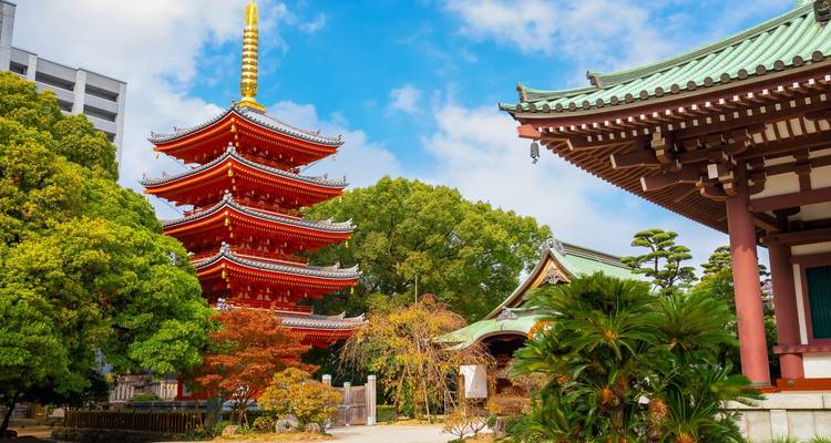 Rote fünfstöckige Pagoda und Tempelstrukturen umgeben von üppigem Grün unter strahlend blauem Himmel.