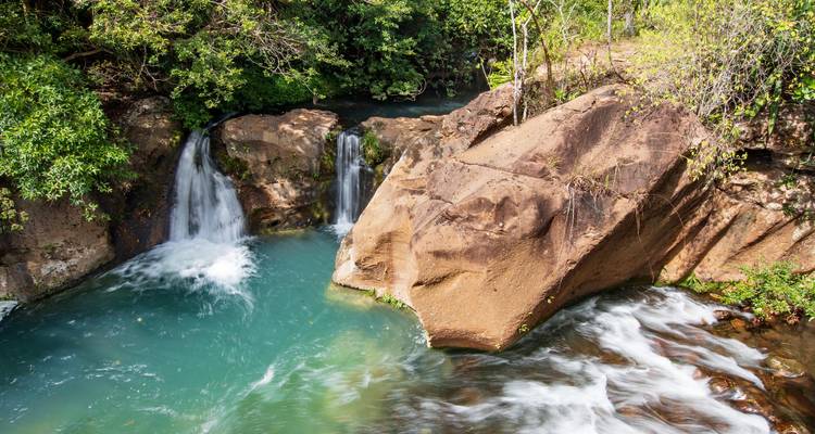 Des cascades jumelles se déversent dans un bassin bleu clair à côté de rochers de jungle moussus.
