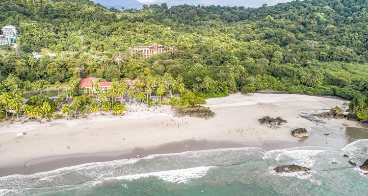 Aerial shot of forest-backed beach with gentle waves in Manuel Antonio National Park.
