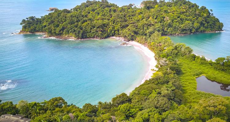 Turquoise waters embrace a lush green peninsula forming a perfect crescent cove.