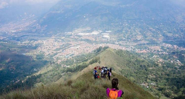 Un groupe descend une crête herbeuse avec vue panoramique sur une vallée colombienne et la ville en contrebas.