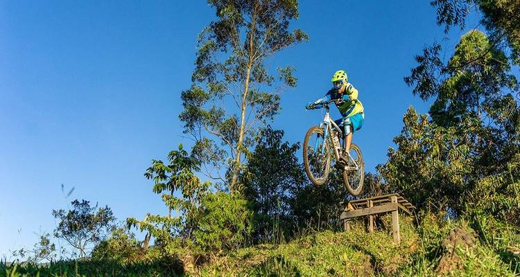 Vététiste en plein vol sautant d'une rampe en bois contre un ciel bleu clair et de grands arbres