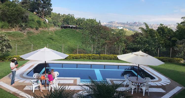 Piscine au sommet d'une colline avec chaises longues blanches et parasols surplombant une vallée verdoyante et une ville au loin