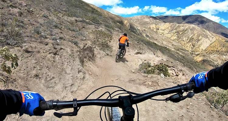 Staubiger Singletrail auf einem trockenen Berghang mit einem Radfahrer voraus unter strahlend blauem Himmel