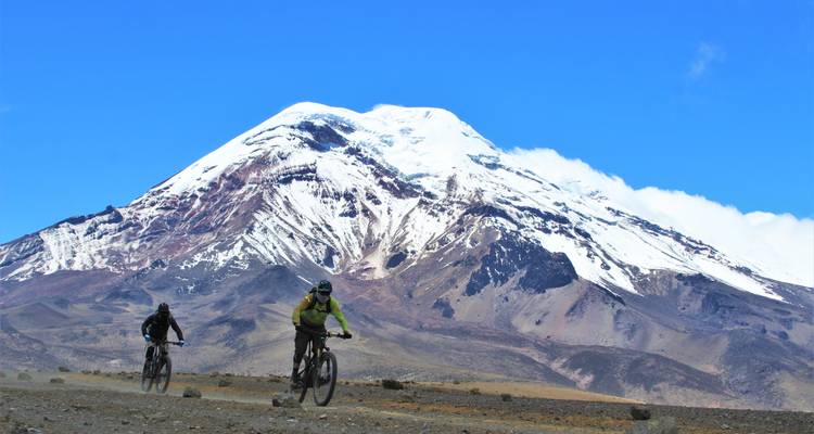 Zwei Radfahrer fahren unter dem schneebedeckten Vulkan Chimborazo vor einem klaren blauen Himmel