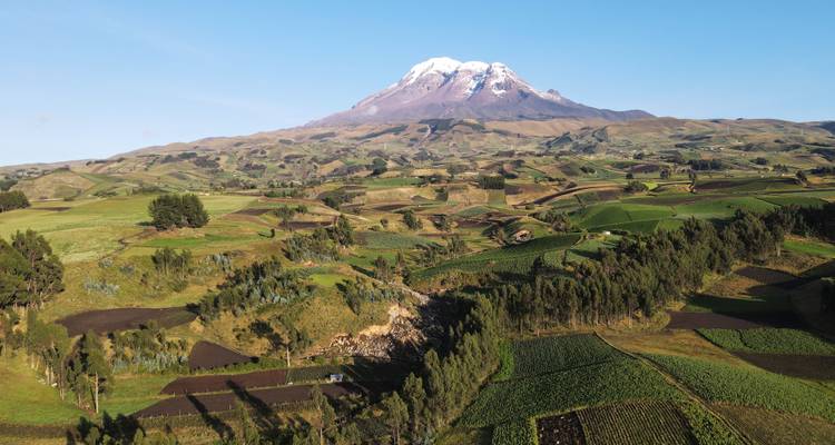 Weite Luftaufnahme von grünem Flickenteppich-Ackerland mit dem schneebedeckten Vulkan Chimborazo, der darüber aufragt