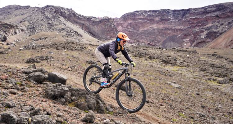 Radfahrer, der zerklüftetes vulkanisches Terrain hinunterfährt mit dramatischen Kraterwänden im Hintergrund